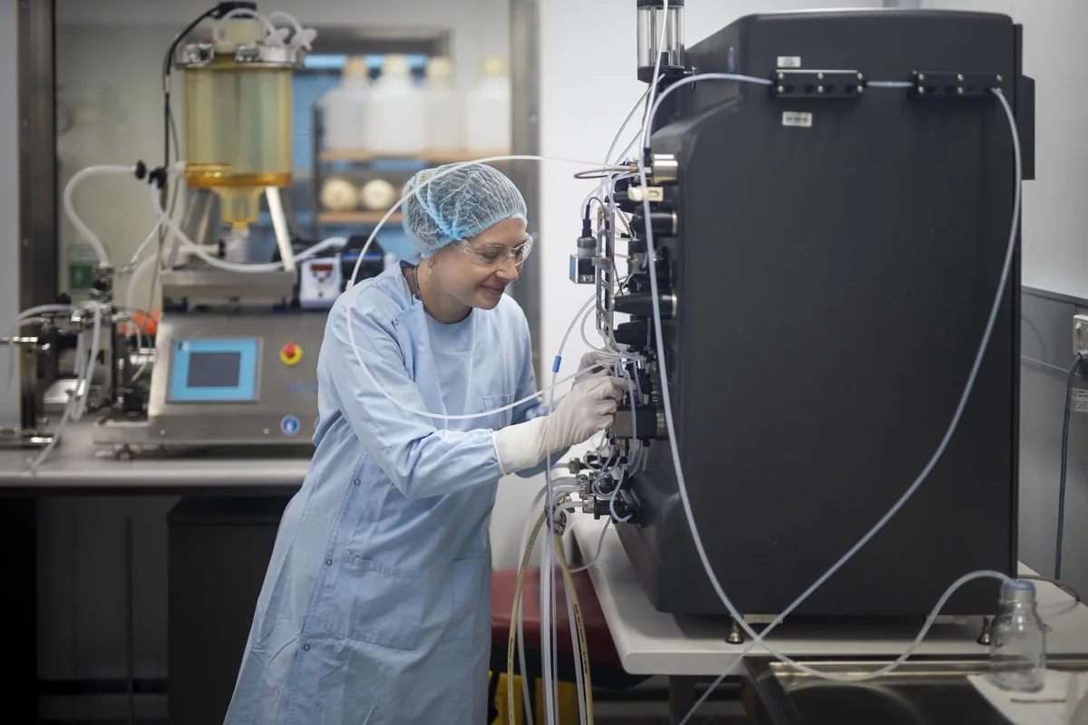 A researcher in cleanroom gown, hairnet and gloves operating manufacturing equipment at the National Biologics Facility